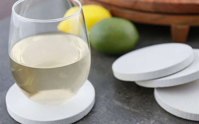 White wine glass resting on a pale sandstone coaster beside citrus